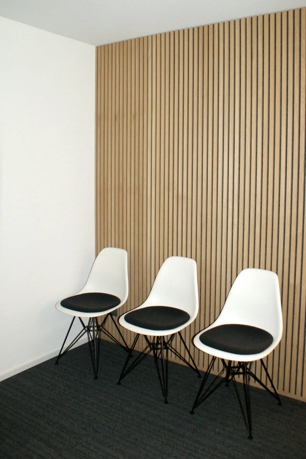 3 chaises devant un revêtement acoustique avec une apparence de lattes de bois.